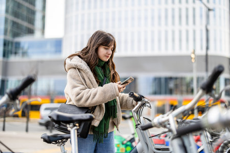 Young woman using mobile phone while standing with bicycle in the city.の写真素材