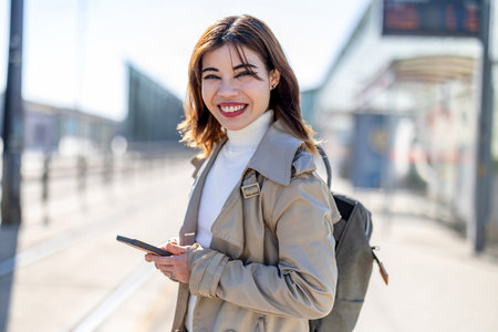 Portrait of a happy young woman using mobile phone at train stationの写真素材