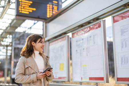 young beautiful and happy woman at train station waiting for train at railway station using mobile phoneの写真素材