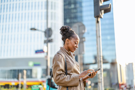 young african american woman walking in city with mobile phone in handsの写真素材