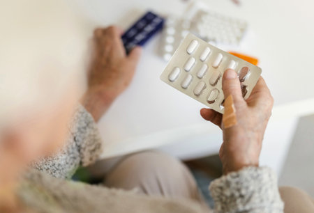 Senior woman taking pills at home, focus on foreground, shallow depth of fieldの写真素材