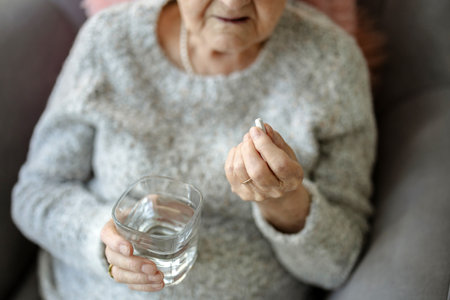 Close up of senior woman holding pills and glass of water at homeの写真素材