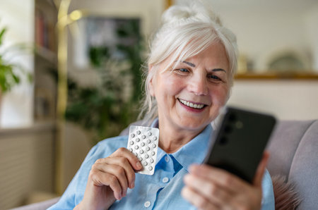 Smiling senior woman using mobile phone while holding blister pack of pillsの写真素材