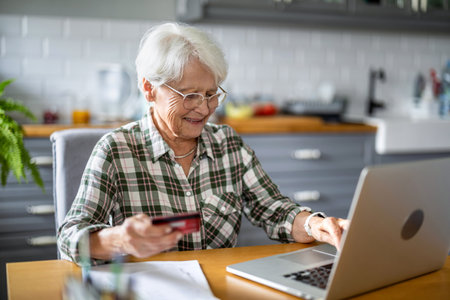 Senior woman shopping online with credit card and laptop in kitchen at home