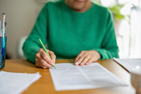 Senior woman signing a document at home. Close-up of an elderly woman signing a document.