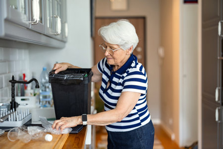 Elderly woman putting garbage into a trash can in the kitchen