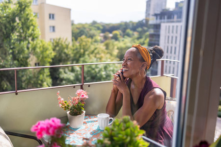 lifestyle portrait of young attractive and happy black afro American woman drinking coffee at home balconyの写真素材