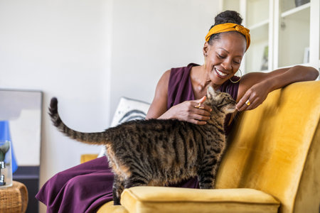 Portrait of smiling woman petting cat while sitting on sofa at homeの写真素材