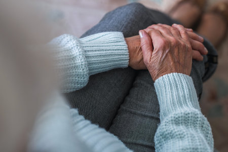 Close-up of senior woman holding her hands while sitting on sofa at homeの写真素材