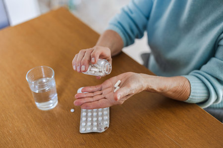 Close up of senior woman holding pills and glass of water at homeの写真素材