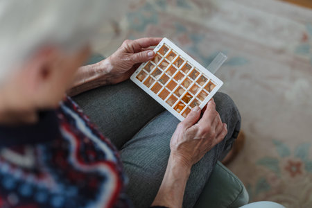 Close-up of senior woman holding pills in her hands while sitting at homeの写真素材