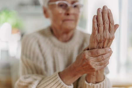 Close up of senior woman holding her hands together while sitting at homeの写真素材