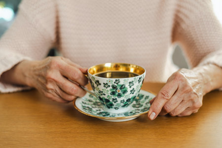 Elderly woman holding a cup of coffee at the table.の写真素材