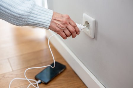 Close-up of senior woman plugging plug into socket at home