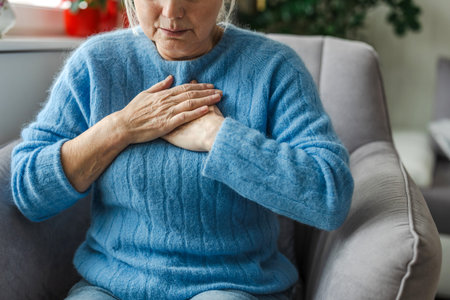 Senior woman suffering from heart attack while sitting in armchair at home