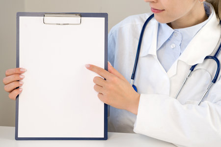 A doctor in a white coat points to an empty space on a paper. The doctor is holding a folder with an empty sheet in his hands. Space for copy and records. medical concept.の写真素材
