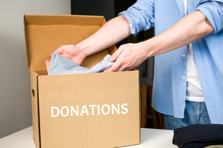 Male Volunteer puts clothes into donation box. Cardboard box with clothes for charity. Help the...