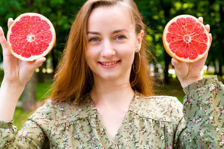 Closeup summer portrait with red haired smiling girl holding grapefruit. Diet Refreshing conceptの写真素材