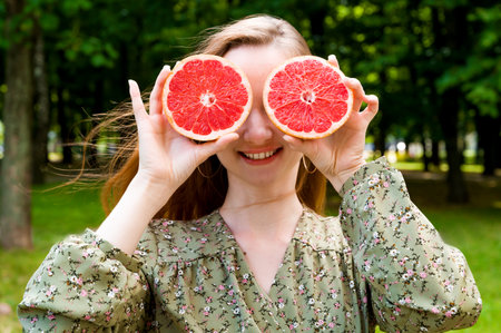 Funny young woman holding juicy grapefruit in front of her eyes. summer portrait outdoors.