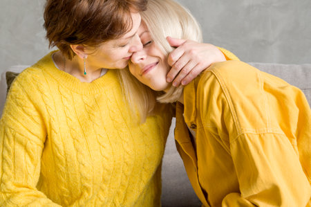 Mother hugging her adult daughter while sitting on the couch. Family relationshipshipsの写真素材