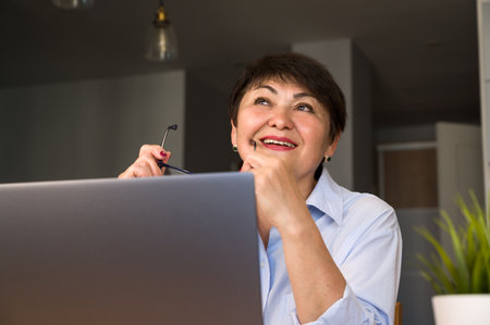 distracted dreamy senior woman sitting at the table with laptop.modern technologies possibilities conceptの写真素材