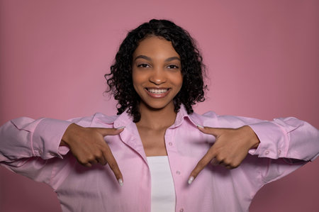 Casual portrait of happy,cheerful African American pointing to the bottom. Promotion and advertising banner. Monochrome pink banner. Valentines day,8 march etc. High quality photoの写真素材