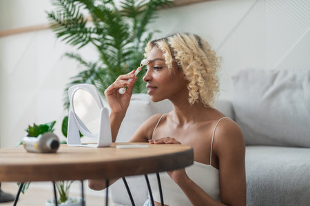 Side view on African American girl doing skin treatment at home. Woman using jade roller for skin care, rejuvenation, relaxation.の写真素材