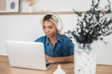 young pretty woman sitting at desk, using laptop to work remotely, taking notes, watching tutorial, lecture or webinar, studying online at home looking at screenの写真素材