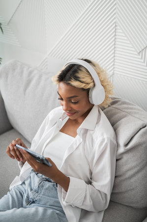 Streaming service and online content concept. Top view on happy girl on the couch in headphones using smarphoneの写真素材
