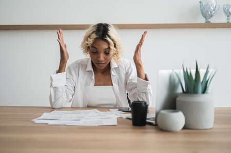Broke,Frustrated african american girl holding her head sitting in fron of pile of bills and invoices.Expenses,cost of living,debt concept.の写真素材