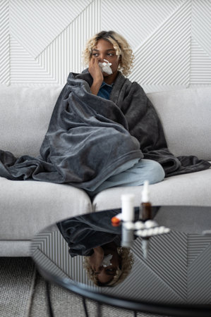 Young ill woman sitting on the couch under the blanket coughing and sneezing.Flu and cold seasonの写真素材