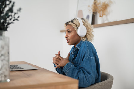 side view on African American woman in headphones video calling on laptop.teacher ot tutor holding online lesson. Adult person having online job interviewの写真素材