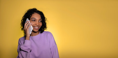 Cheerful young african american girl posing isolated on yellow wall talking on the phone People...