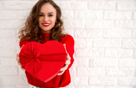 Closeup of a heart shaped gift with in hands of a young smiling woman. Valentine's,birthday,anniversary etc.Copyspace banner.Focus on the boxの写真素材