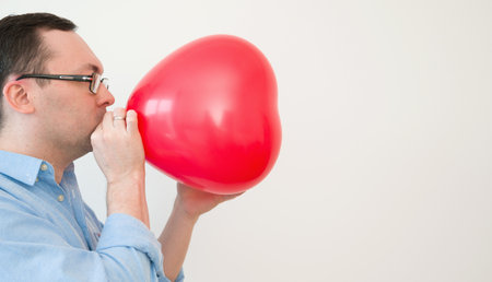 Side view on a man blowing heart balloon preparing for valentines day or anniversary