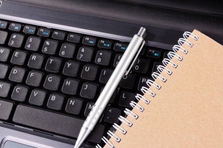 a pen and notebook lie on the keyboard of computerの写真素材