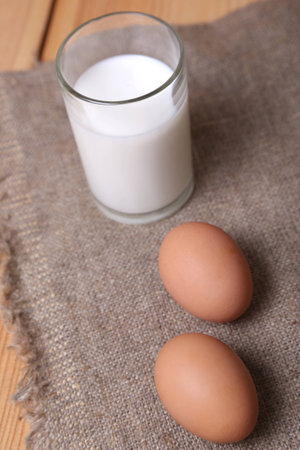 glass with milk and a few eggs on fabricの写真素材