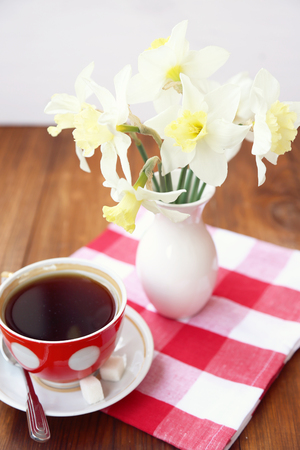 few narcissuses are in a vase, alongside cup with teaの写真素材