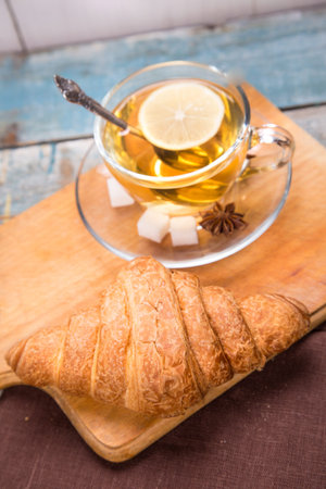 one fresh croissant,hot tea with a lemon in a studioの写真素材