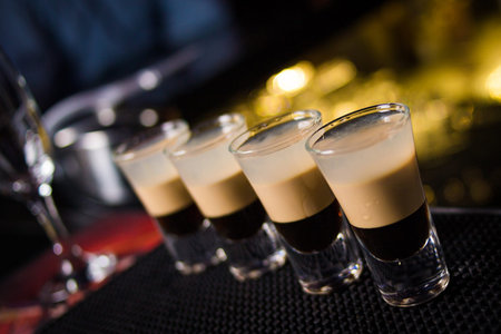an alcoholic brown layered cocktail is in beautiful glass, on the bar