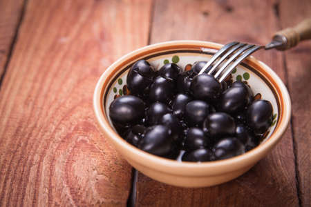 black olives with fork, on a wooden backgroundの写真素材