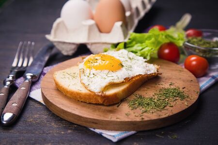 fried egg with dry dill and vegetables on wooden plateの写真素材