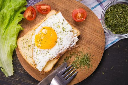 fried egg with dry dill and vegetables on wooden plateの写真素材