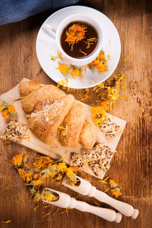 fresh tea with croissant and calendula on wooden backgroundの写真素材