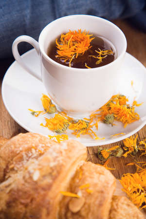 fresh tea with croissant and calendula on wooden backgroundの写真素材