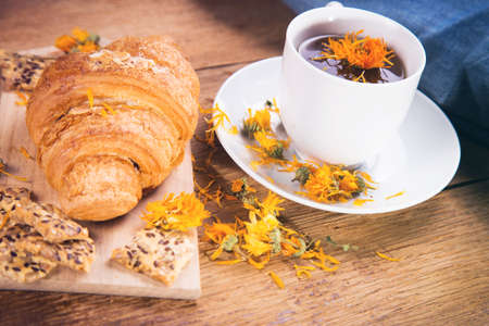 fresh tea with croissant and calendula on wooden backgroundの写真素材