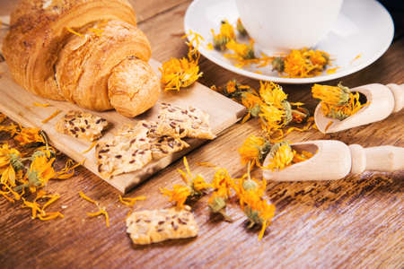 fresh tea with croissant and calendula on wooden backgroundの写真素材