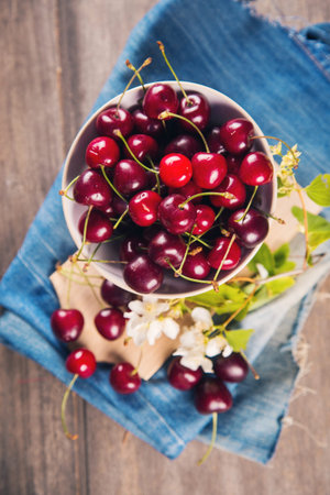 ripe raw dark red cherrys with white flowers on blue textile