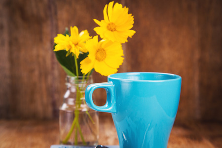 blue cup with fresh coffee and yellow flowers in glass containerの写真素材