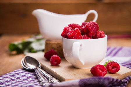fresh ripe raspberry in white cup with jam on wooden background